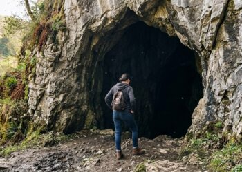 Person standing at the entrance of a dark cave, hesitating before stepping inside