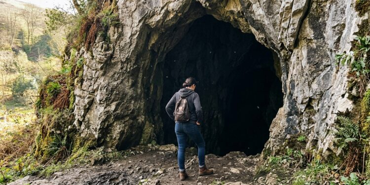Person standing at the entrance of a dark cave, hesitating before stepping inside