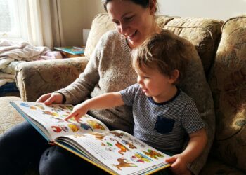 Parent and young child reading a colorful question-and-answer book together on a couch