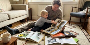 Parent and young child reading colorful nonfiction fact books together on a rug
